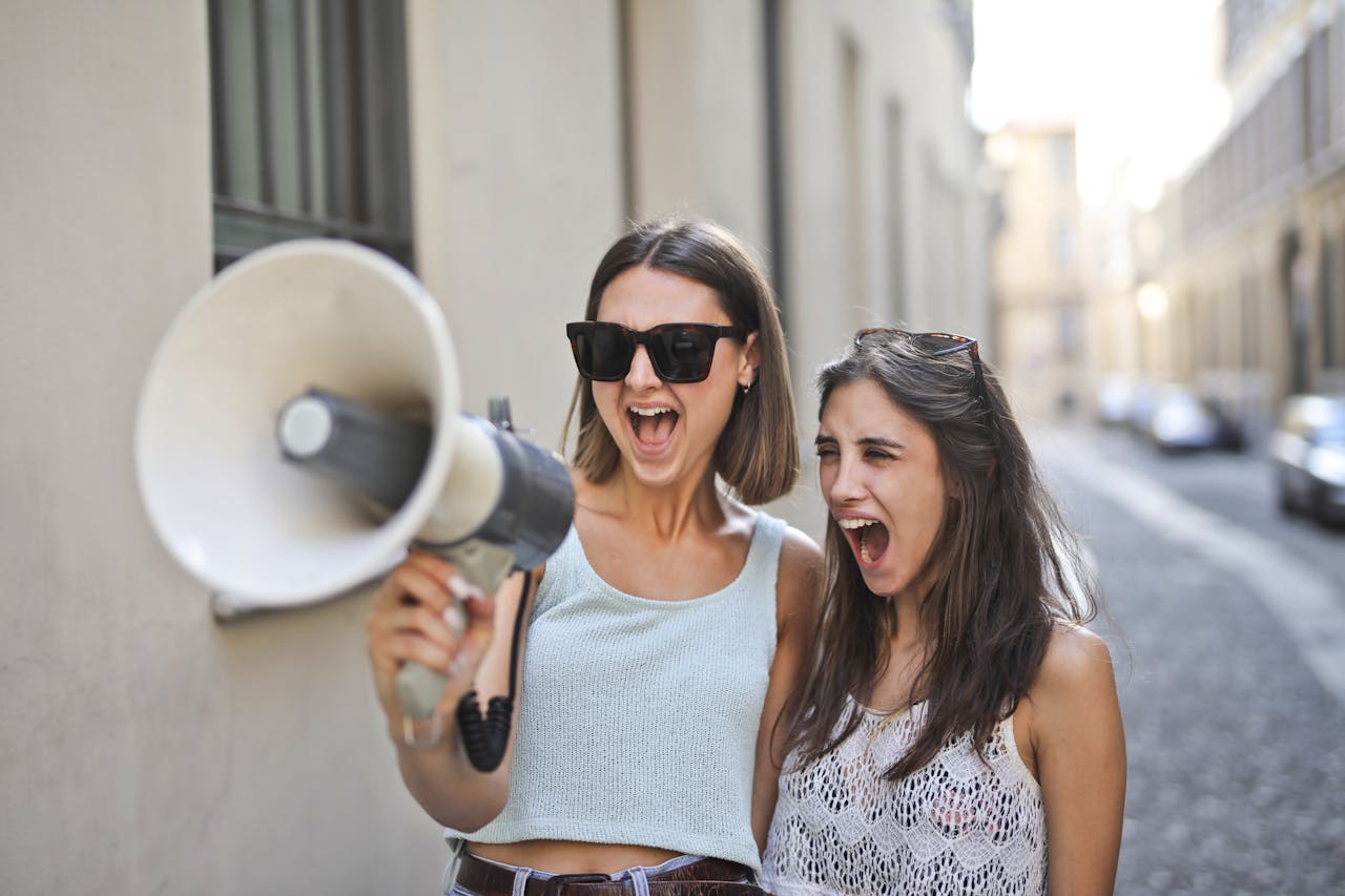 Two cheerful women expressing joy and excitement outdoors with a megaphone.